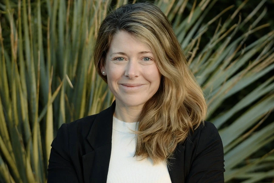 woman with brown hair in black blazer smiling with huge plant in backdrop